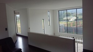 A spacious room with large windows offering a view of a residential area. - Comfort Campestre (Tabio)