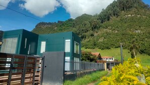 A modern building with a green facade, surrounded by lush greenery and hills. - Comfort Campestre (Tabio)