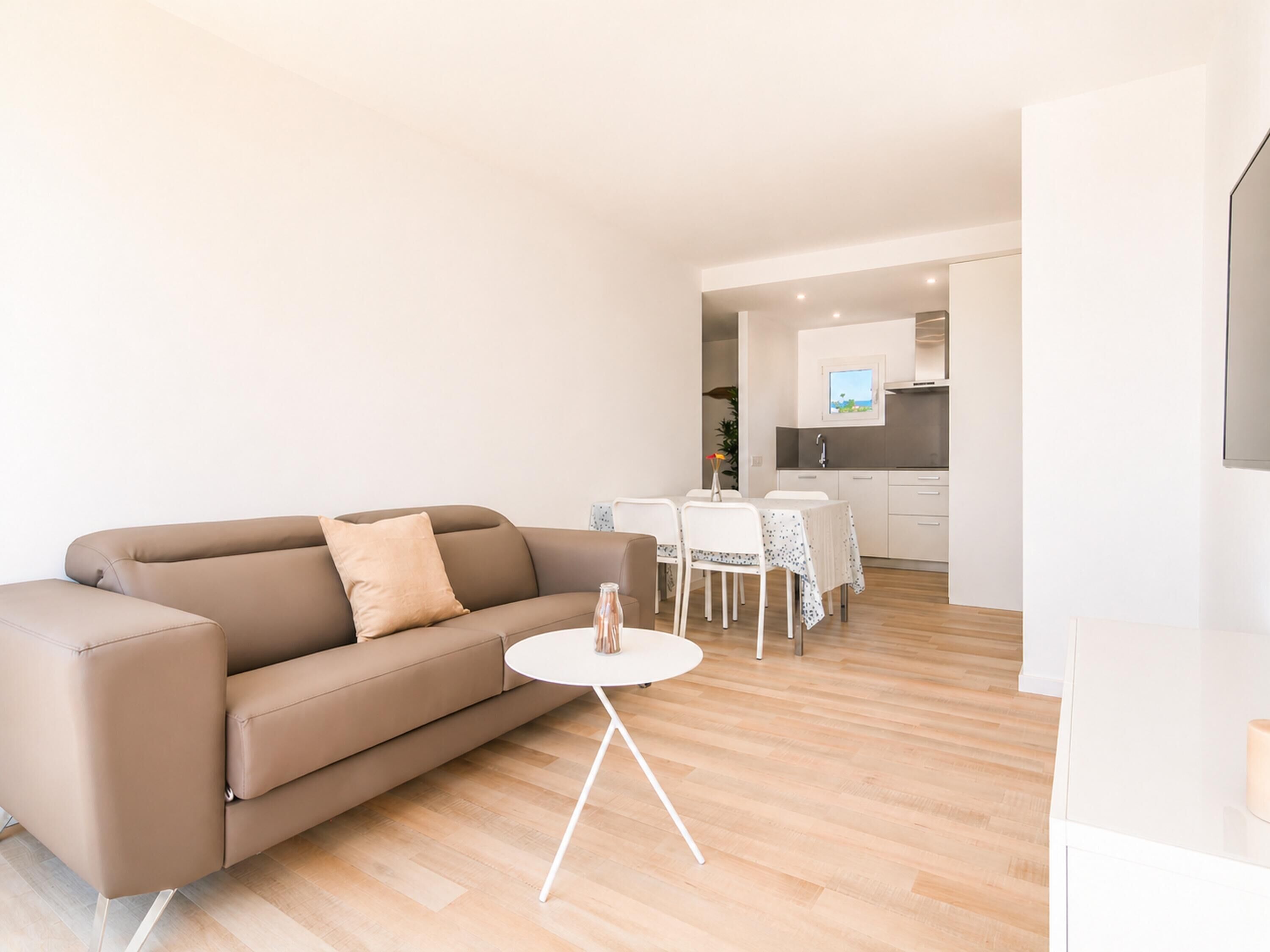 A modern living room with a sofa, a small round table, and a dining area with a table and chairs.