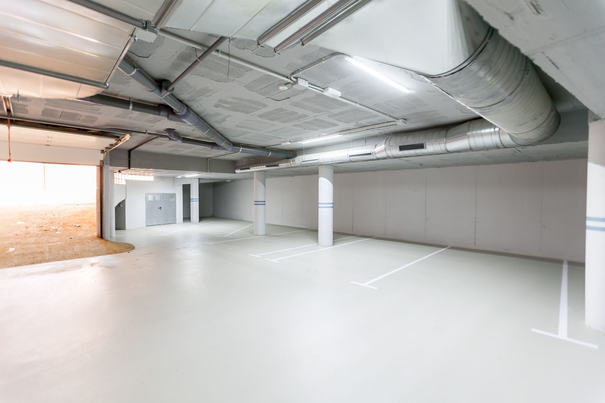 An empty parking garage with white walls, concrete floors, and visible ductwork on the ceiling.