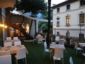 An outdoor dining area with tables and chairs, surrounded by greenery and a building with classical architecture. - Hotel Firenze Lugano (Lugano)