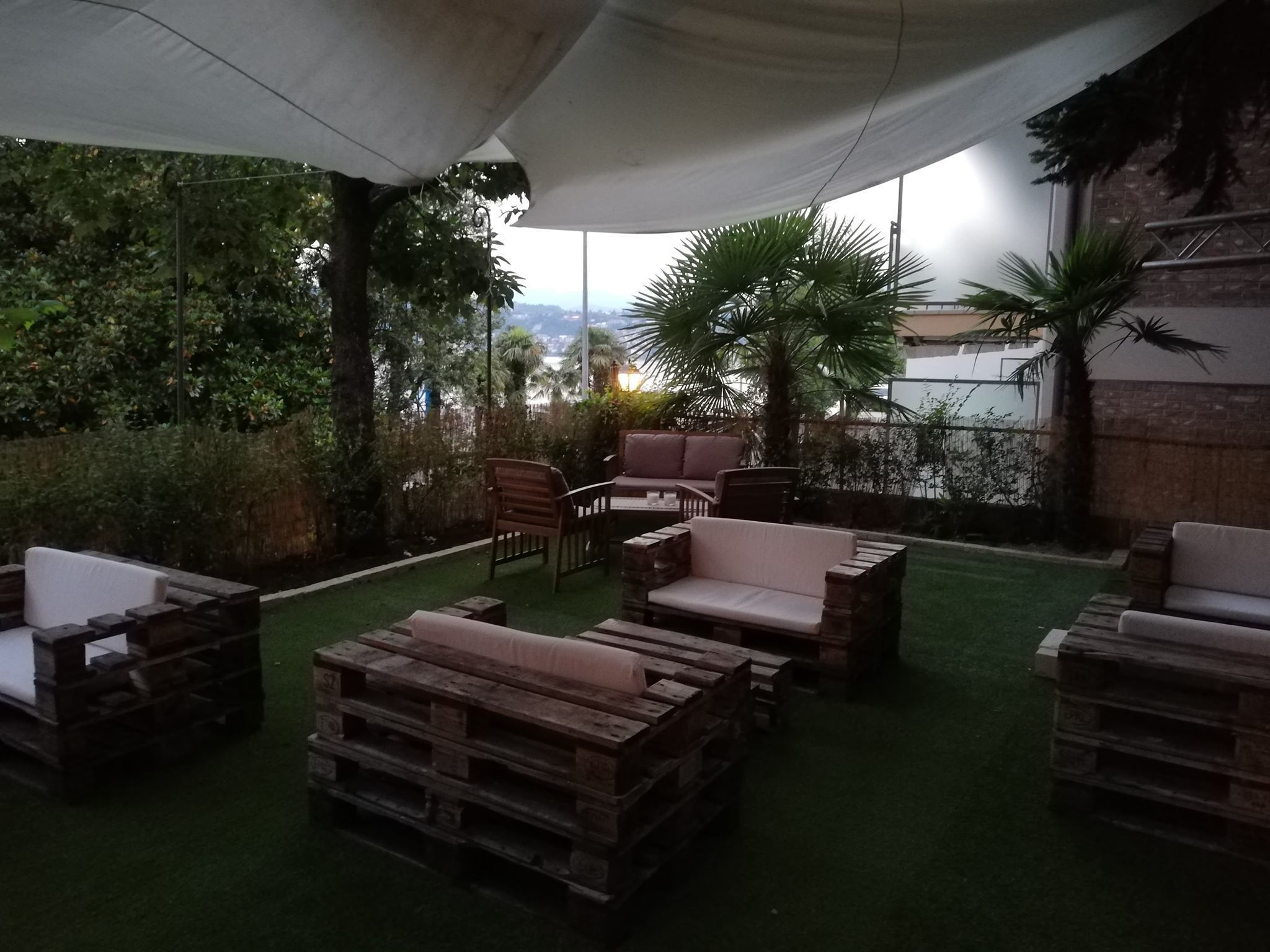 Un área de estar al aire libre con mobiliario de madera y un toldo blanco.