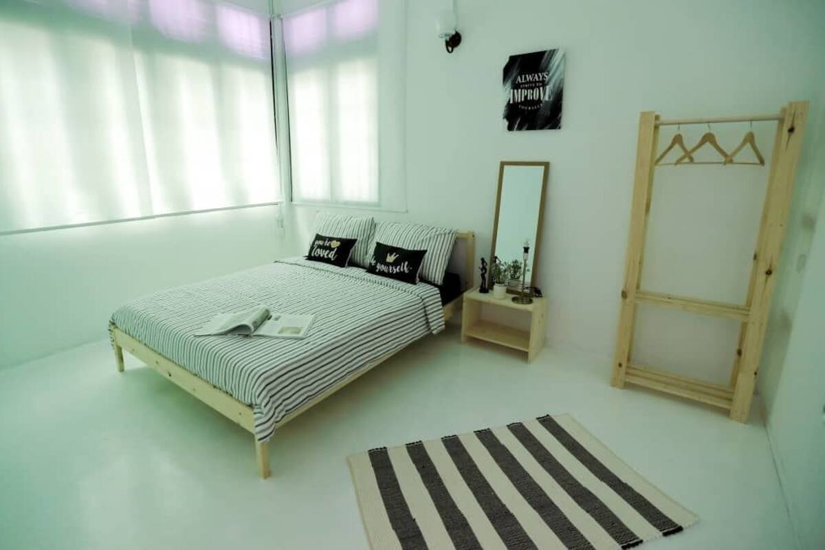 Une chambre à coucher avec un lit, une table de chevet, un miroir, une armoire en bois, un tapis à rayures et une affiche motivante accrochée au mur.