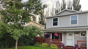 Une maison à deux étages avec un porche à l’avant, un petit jardin et une clôture rouge.