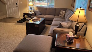 Un salon comprenant un canapé, un pouf, une table basse, une lampe et une porte ornée d’un vitrail.