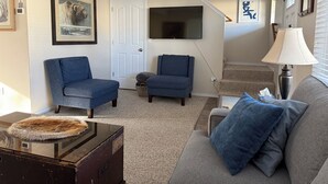 Un salon avec deux canapés, un téléviseur, une lampe et un escalier.