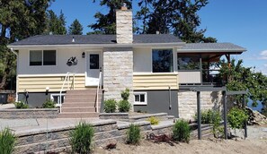 Une maison à deux étages, dotée d’une façade en pierre, d’un porche couvert et d’un petit jardin à l’avant, avec des marches menant à l’entrée.