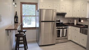 A modern kitchen with white cabinets, stainless steel appliances, a window with a view, and bar stools.