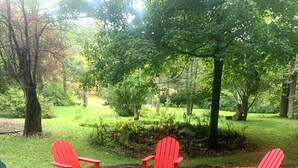 A patio with red and green Adirondack chairs arranged in a circle, surrounded by a stone-tiled area with a view of a lush garden and trees.
