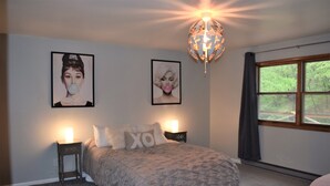 A bedroom with a bed, two bedside tables, a wall-mounted light fixture, and two framed pictures.
