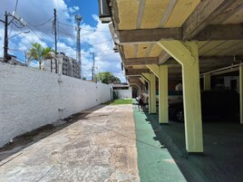 Uma área de estacionamento coberta com piso de concreto, parede branca em um lado e piso pintado de verde no outro.