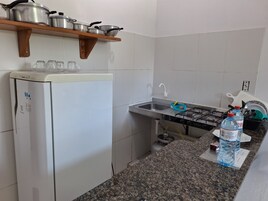 Uma cozinha compacta com geladeira branca, fogão a gás, pia e prateleira de madeira com panelas e frigideiras.