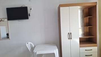 Una habitación con un armario blanco, una silla blanca, un televisor montado en la pared y una cama con ropa de cama blanca.