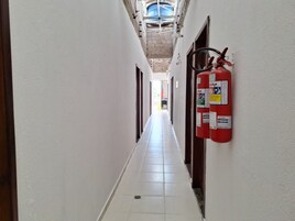 Um corredor com paredes brancas, chão ladrilhado e um extintor fixado na parede.