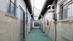 Um corredor estreito com paredes revestidas de azulejos, grades de metal e chão verde.