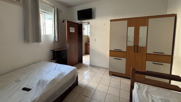 Quarto com cama, escrivaninha, guarda-roupa e televisão na parede.