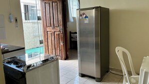 Uma cozinha com fogão, geladeira, porta de madeira e cadeira de plástico branca.