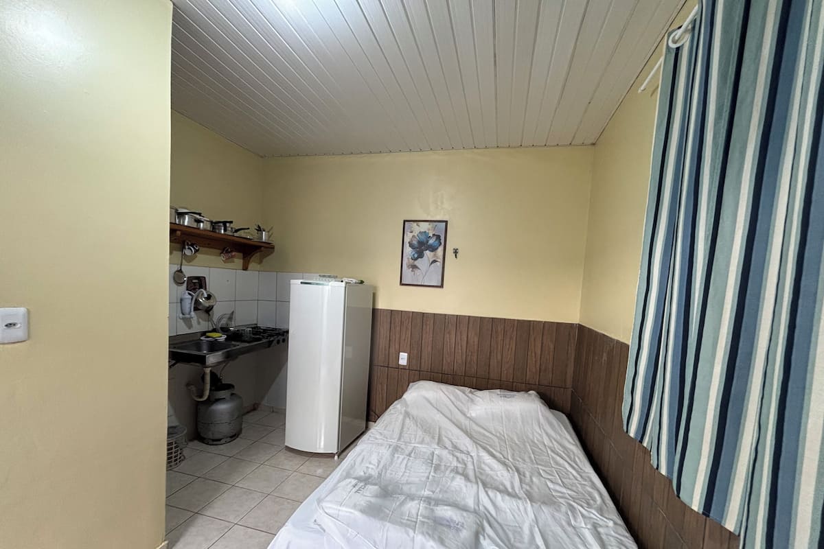 A small, compact room with a bed, a kitchenette, and a shower area.
