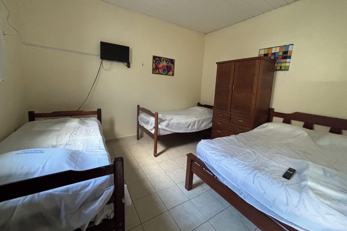 A room with three wooden beds, a wooden wardrobe, a television mounted on the wall, and a colorful painting.