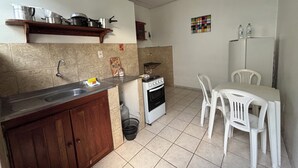 Cozinha compacta com pia, fogão e cadeiras brancas.