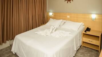 Quarto de hotel com cama bem arrumada, telefone de apoio e ar condicionado fixado na parede.