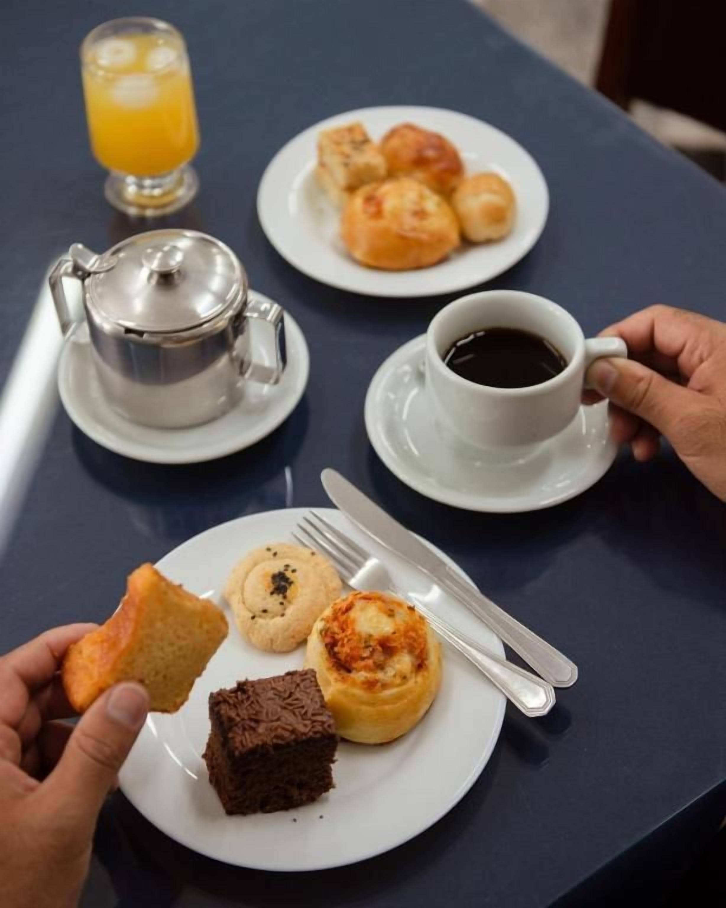 Una mesa con una taza de café, un vaso de jugo de naranja y un plato con pasteles y una pequeña tetera.
