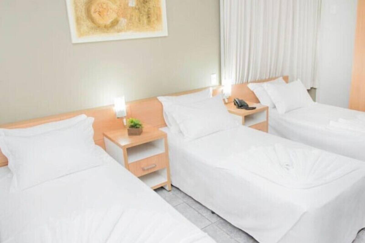 A hotel room with three single beds, each with a wooden nightstand, a lamp, and a phone.