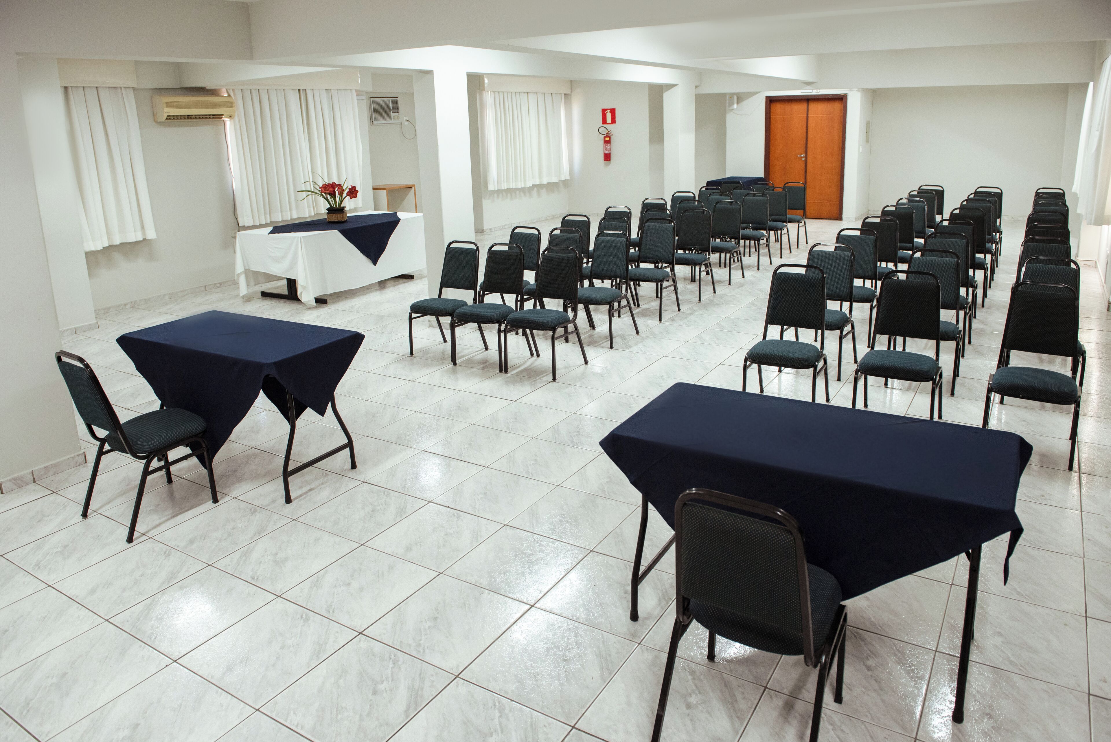 Un salón de conferencias con varias mesas y sillas, paredes blancas y una puerta de madera.