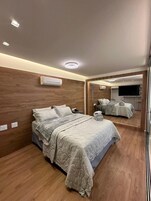 Quarto moderno com cabeceira de madeira, cama grande com edredom acolchoado, mesa de cabeceira e televisão de tela plana na parede.