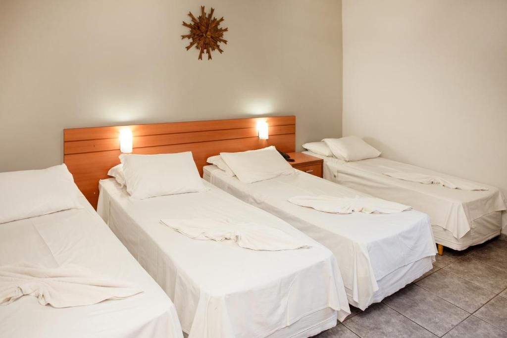 Una habitación de hotel con tres camas individuales, cada una con cubrecama y almohadas blancas.