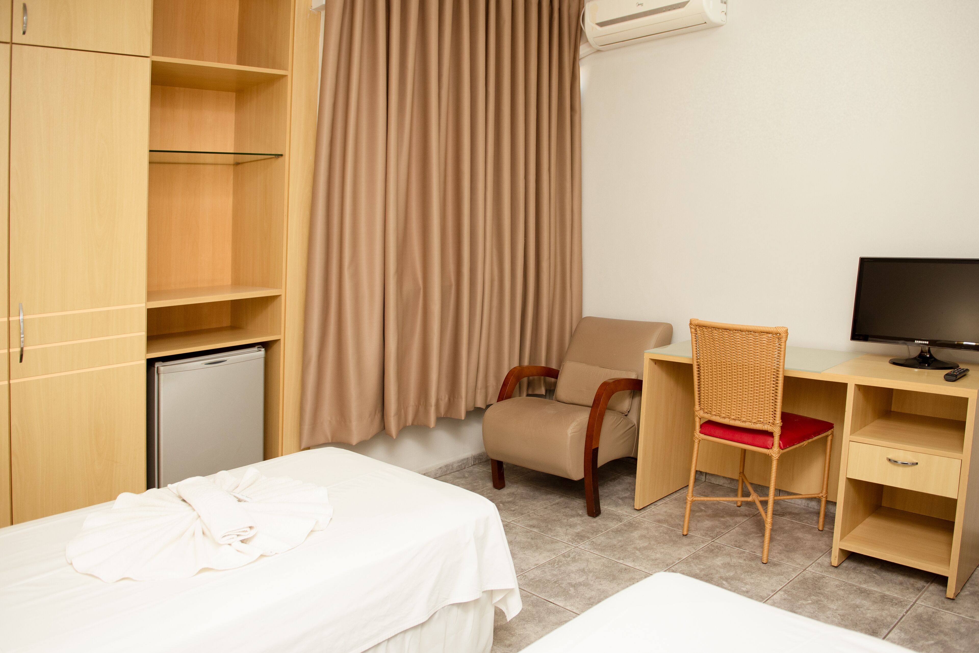 A hotel room with a bed, a desk with a chair, a television, and a wardrobe.