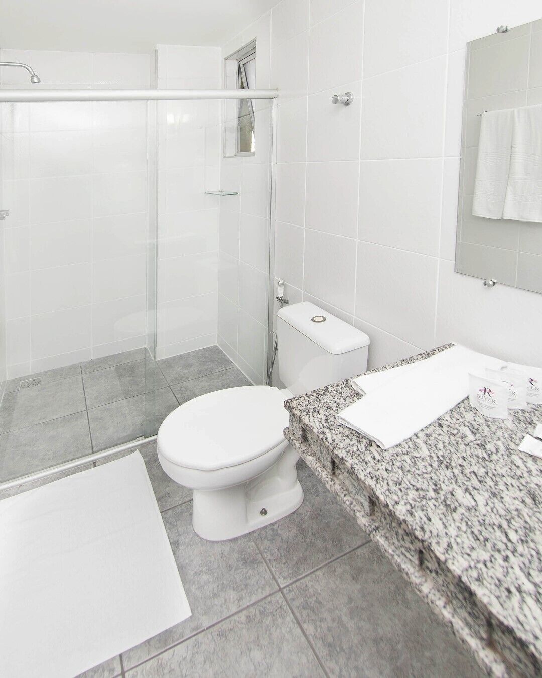 A modern bathroom with a glass shower enclosure, a white toilet, and a granite countertop with a sink and mirror.