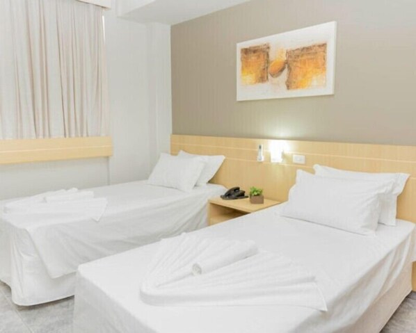A hotel room with two single beds, a nightstand with a phone and a small plant, and a painting on the wall.
