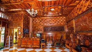 A room with a checkered floor, wooden ceiling with intricate patterns, a chandelier, and ornate furniture.