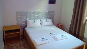 A neatly made bed with two pillows and two folded towels, a wooden nightstand, a small stool, a wall-mounted light, and a framed picture. - Diplomat Diani Beach Resort (Diani Beach)