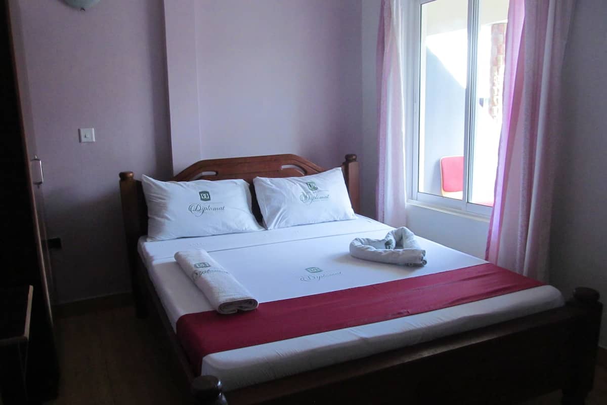 A neatly made bed with a red blanket, white pillows, and a folded towel.