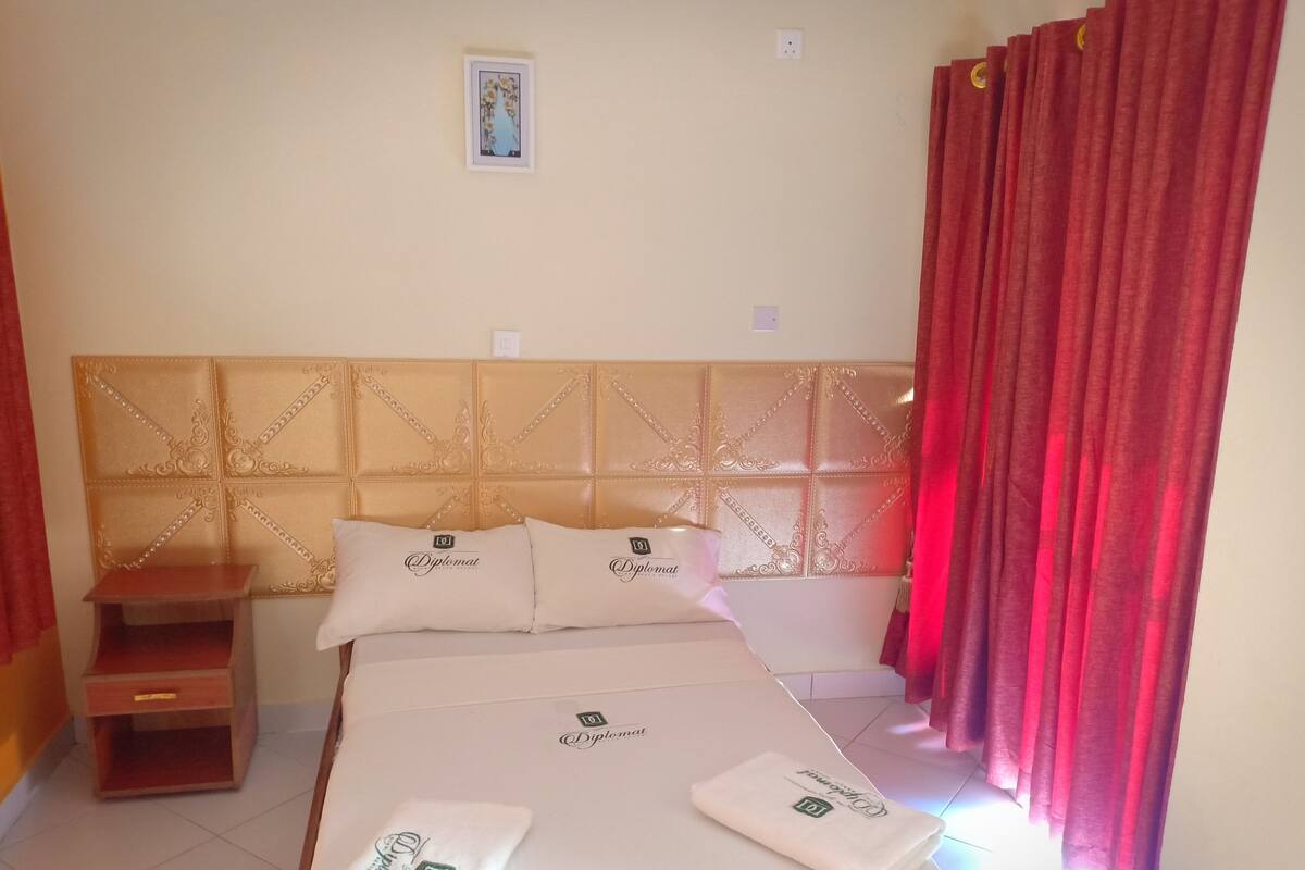 A hotel room with a bed, pillows, a nightstand, and a red curtain.
