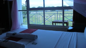 A bedroom with a large window, a bed with a red pillow, and a wooden bench. - Diplomat Diani Beach Resort (Diani Beach)