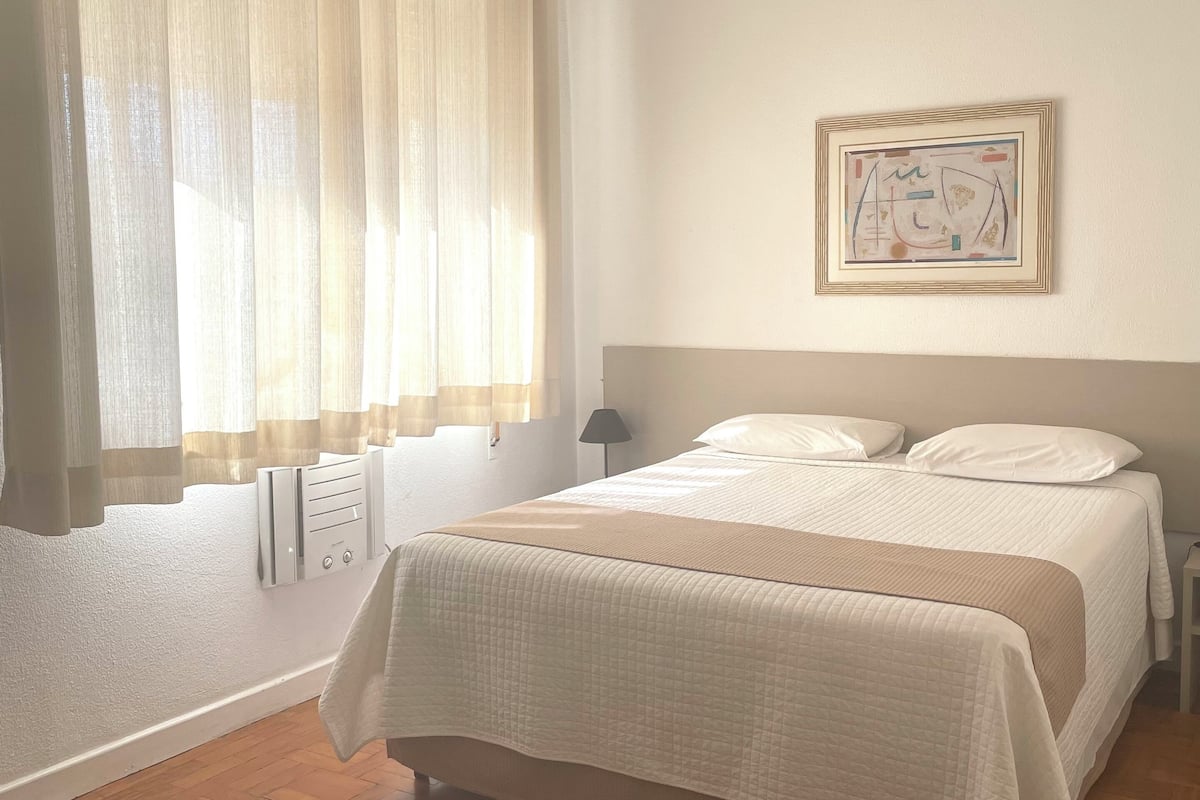 Een slaapkamer met een bed, een radiator, een raam met gordijnen en een aan de muur hangend schilderij.