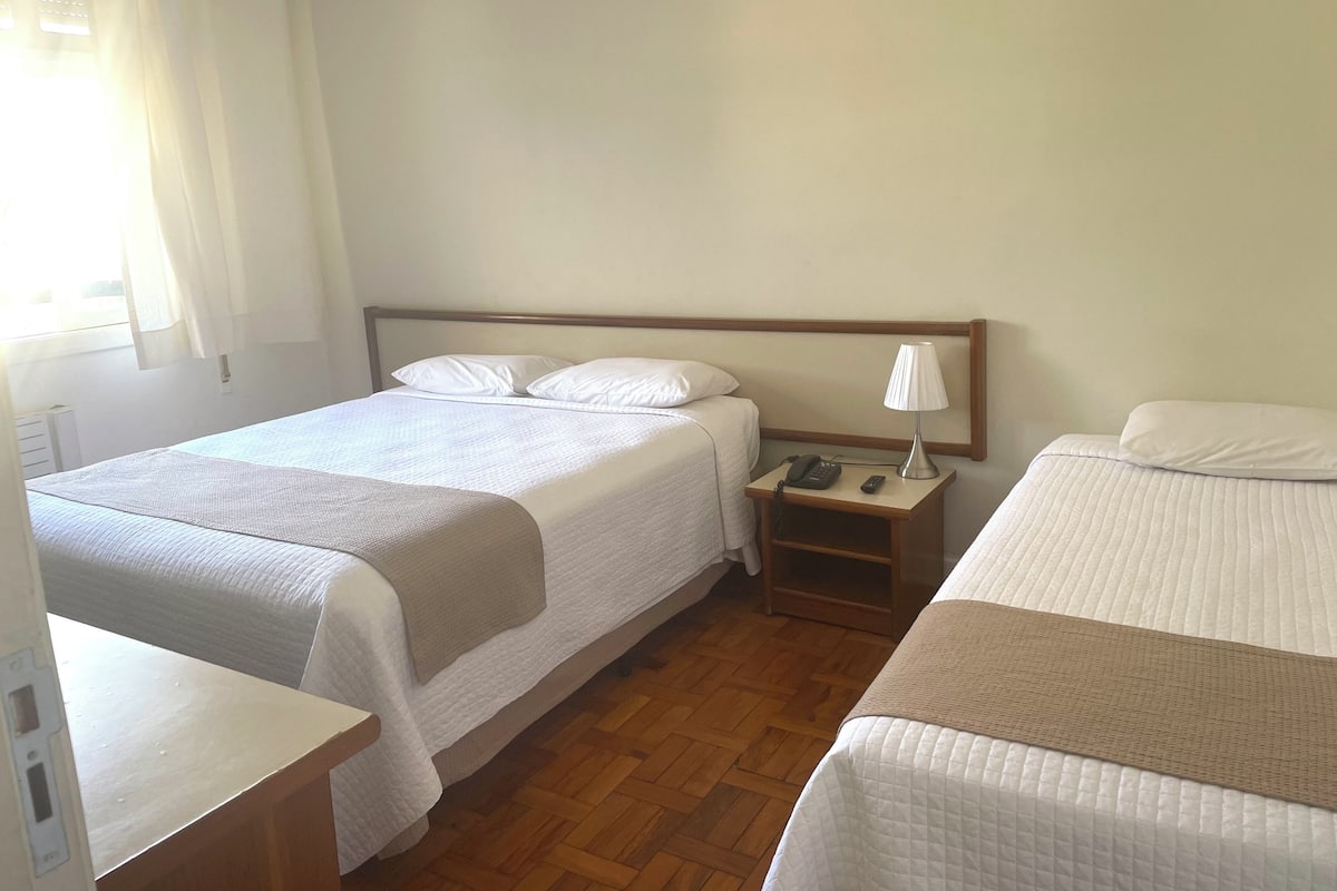 Een hotelkamer met twee bedden, een nachtkastje met een lamp, een telefoon en een houten vloer.