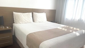 A neatly made bed with white bedding and a beige throw blanket, a bedside table with a lamp, and a wooden headboard. - Grande Hotel Amparo (Amparo)