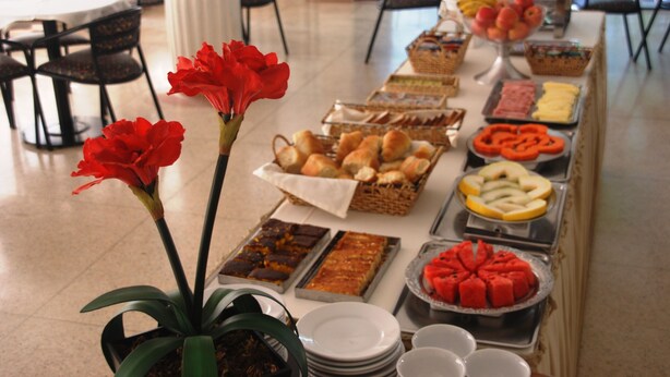A buffet table with various food items and a potted plant with red flowers. - Grande Hotel Amparo (Amparo)