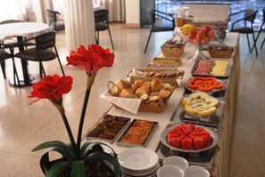 A buffet table with various food items and a potted plant with red flowers. - Grande Hotel Amparo (Amparo)