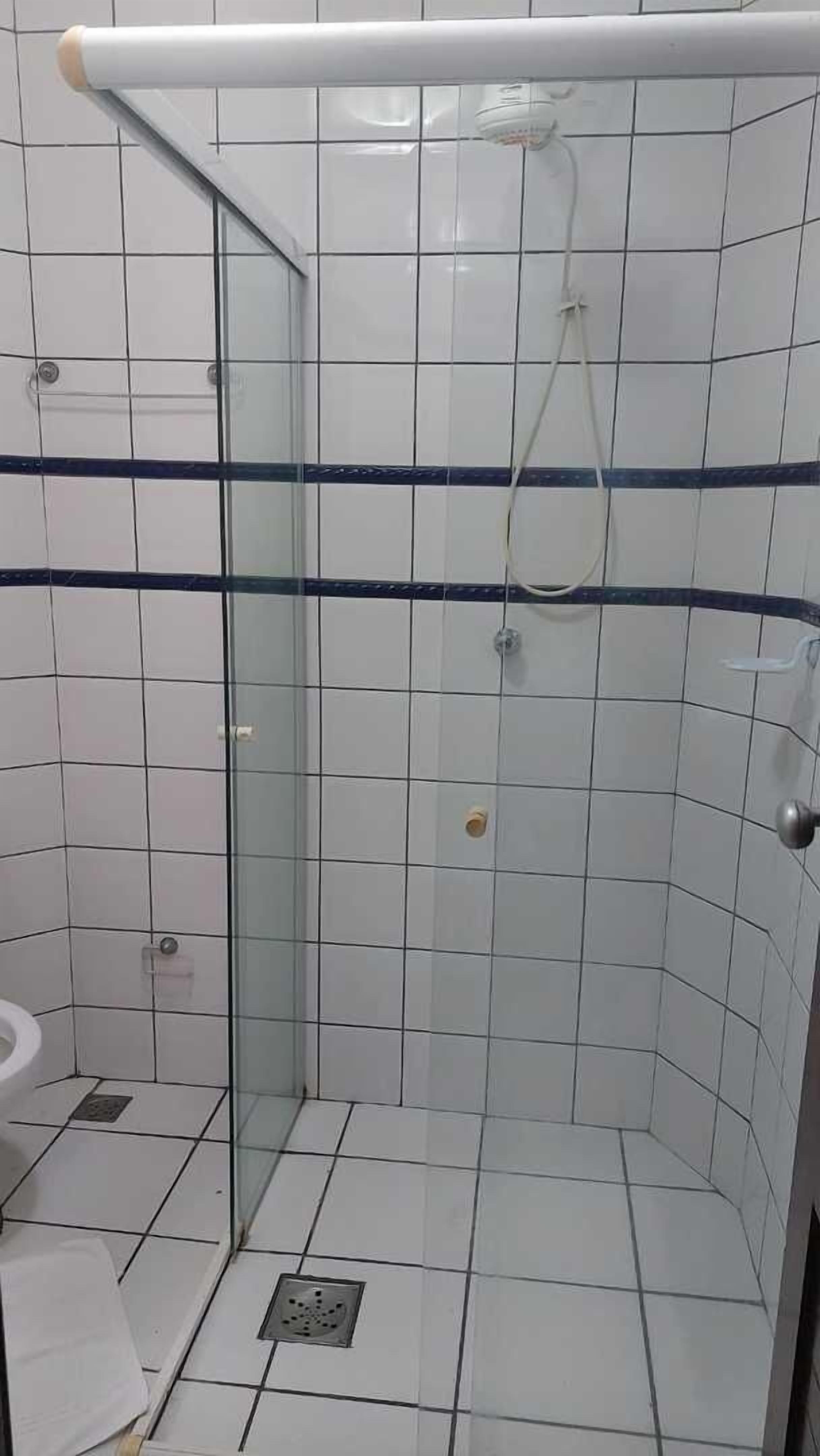 A bathroom with a glass-enclosed shower, white tiles, and a blue stripe.