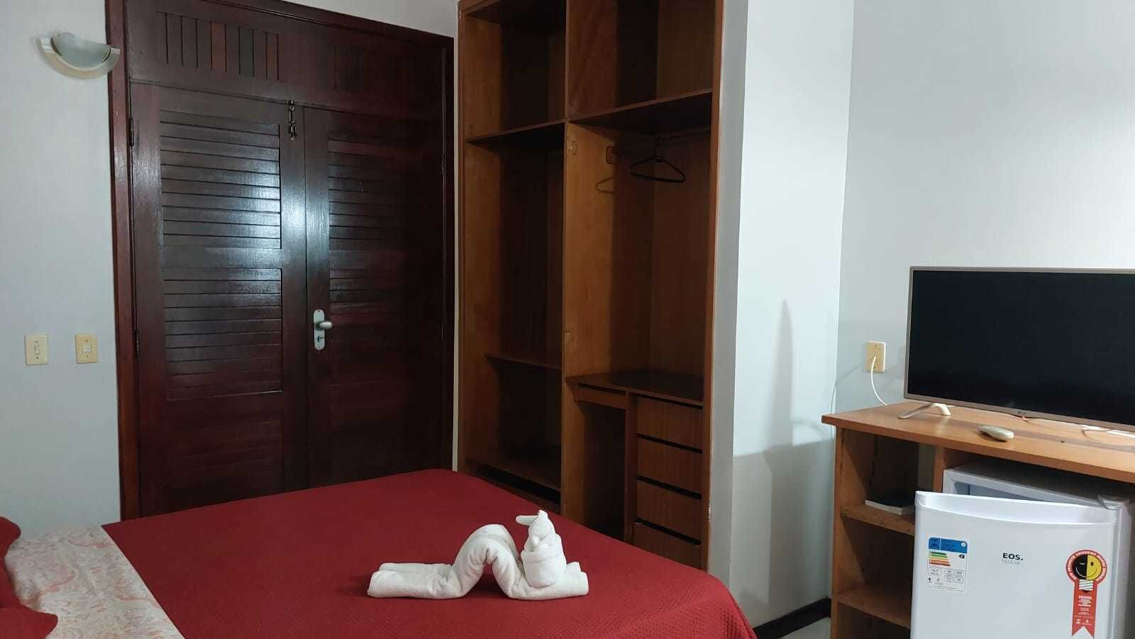 A hotel room with a red bed, wooden wardrobe, and a TV on a wooden stand.