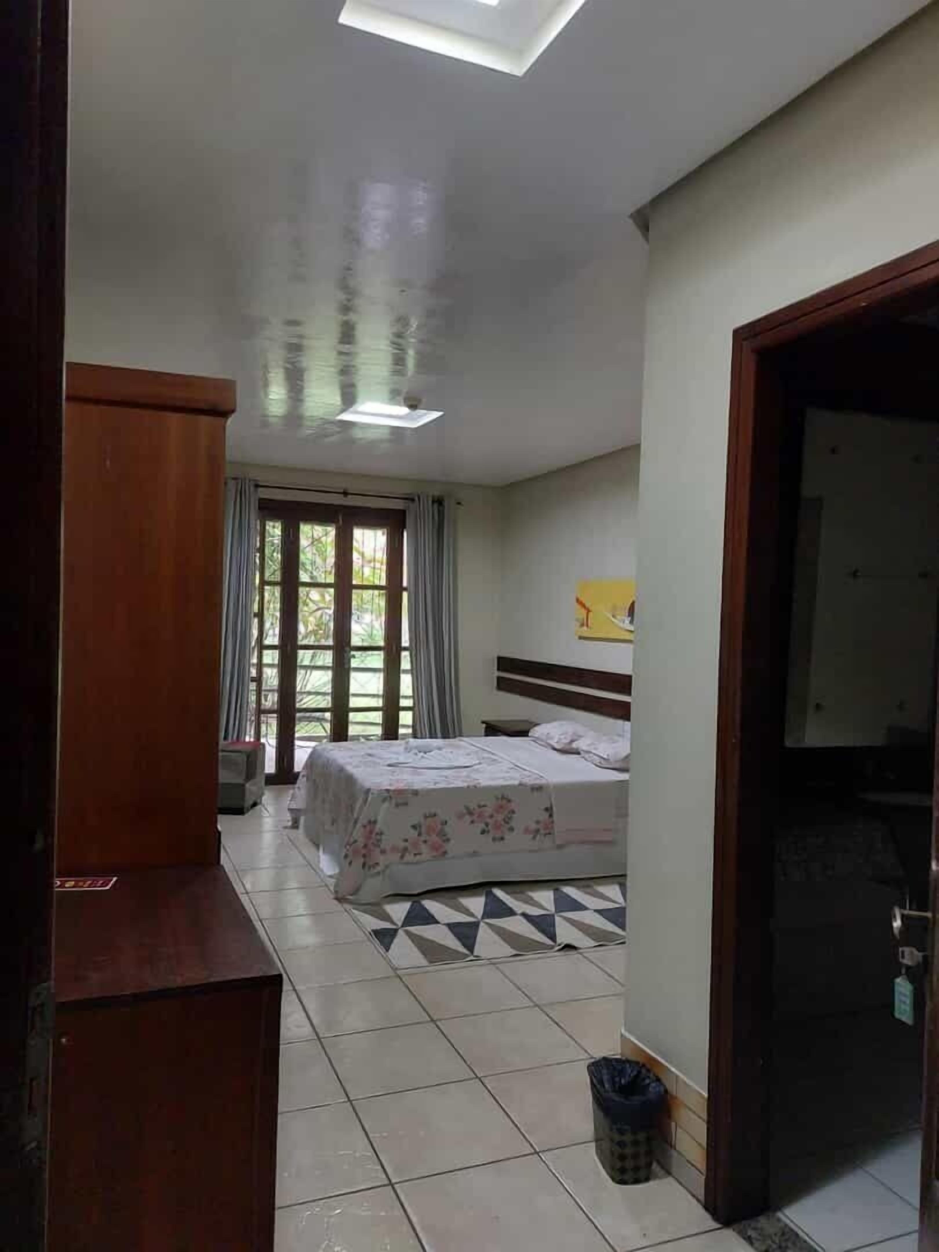 Une chambre à coucher avec un lit, une tête de lit en bois, un luminaire au plafond et une vue par la fenêtre.