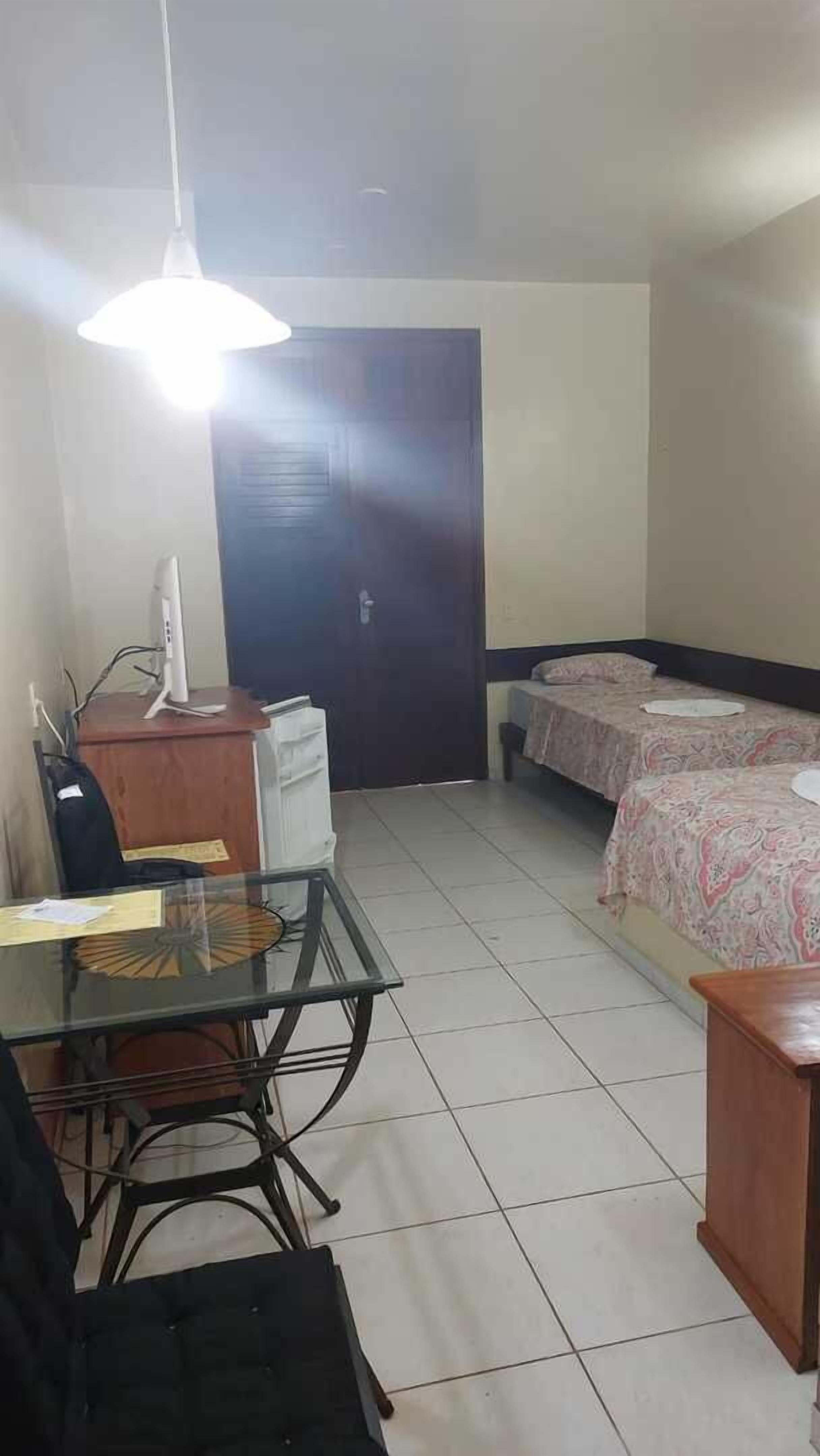 A small, clean room with a desk, chair, two beds, and a door.