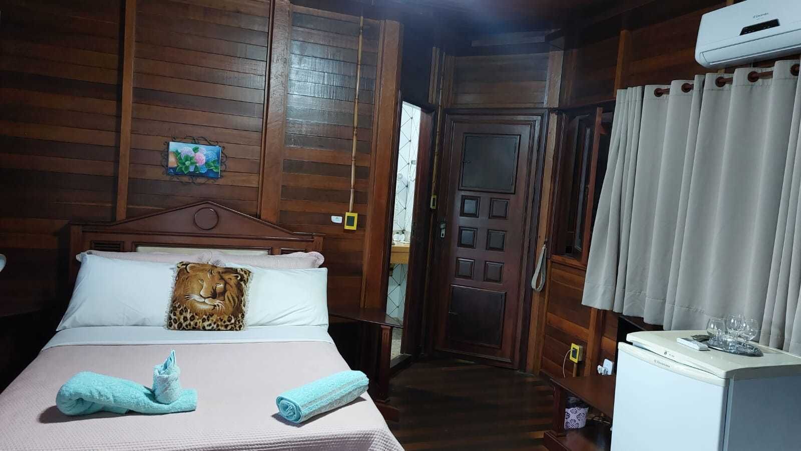 Une chambre d’hôtel avec un intérieur en bois, un lit agrémenté d’un coussin à motifs léopard, une serviette roulée, une table de chevet avec un verre et une porte dotée d’une fenêtre.
