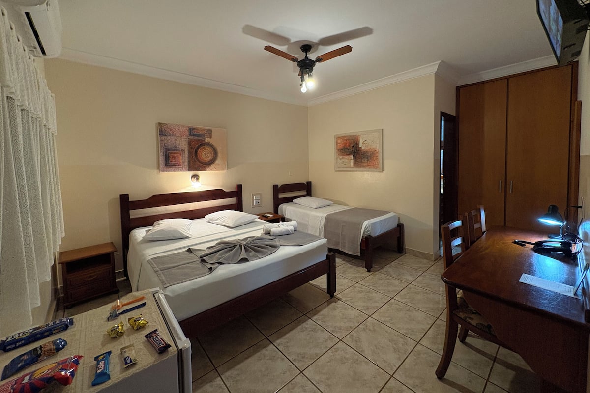 Une chambre d’hôtel avec deux lits simples, un ventilateur de plafond, une table en bois et un bureau avec une lampe.
