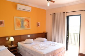 A hotel room with a bed, a nightstand, an air conditioner, and a view of the outside.